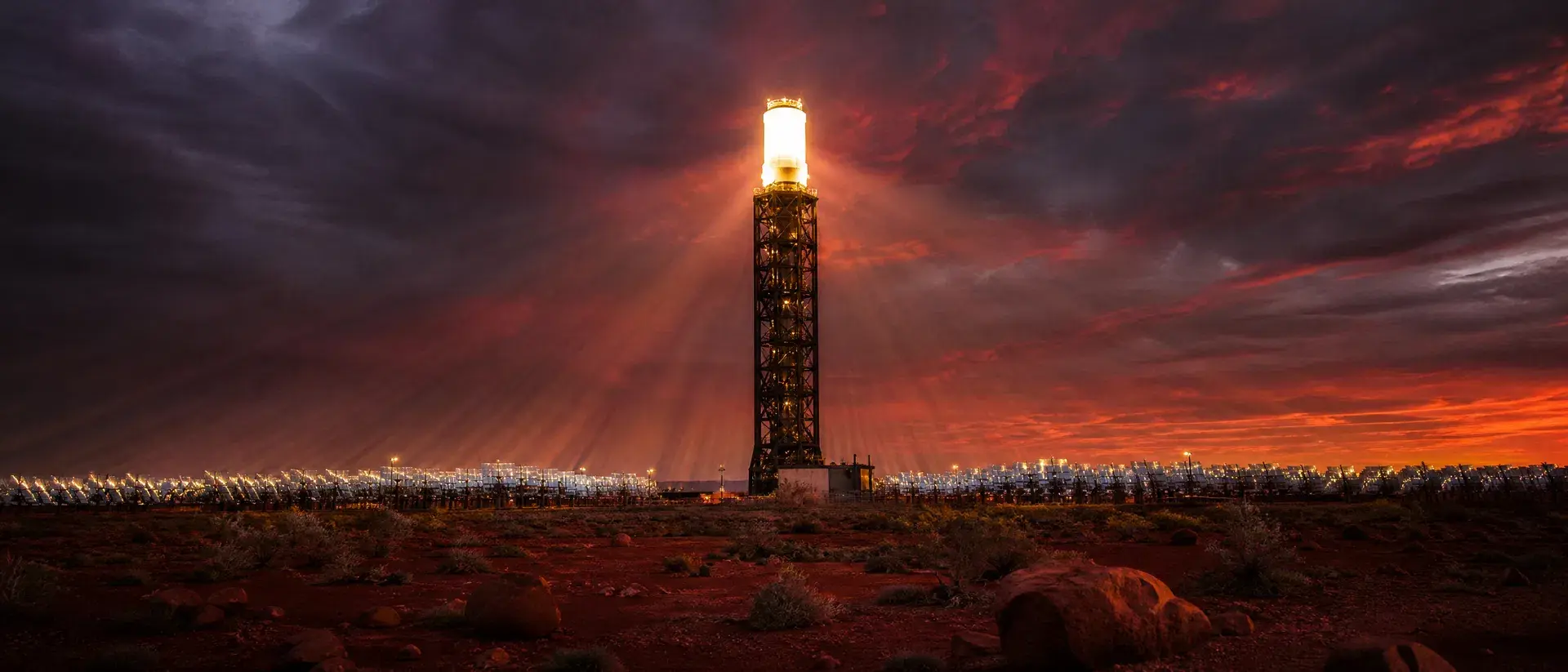 Concept render of a tower receiver glowing at dusk, charging molten-salt storage as the sky darkens